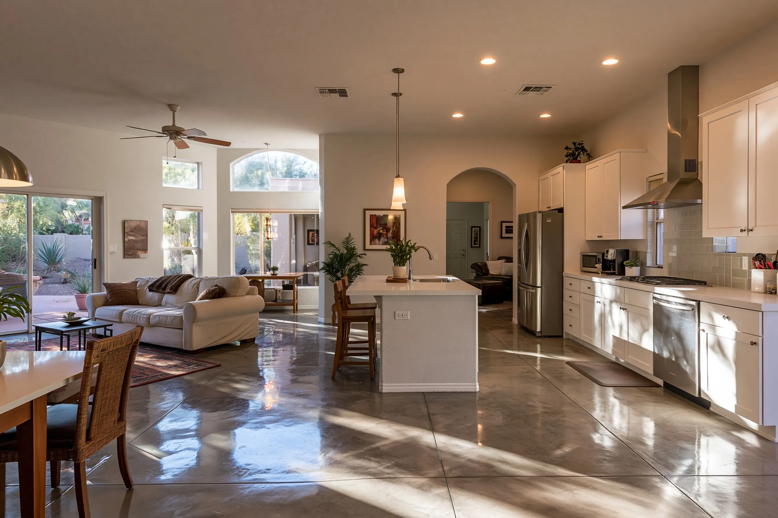 Kitchen and great room of a newer valley house with a warm grey polished concrete floor catching light from a window, white shaker cabinets and stucco walls, nothing on the floor