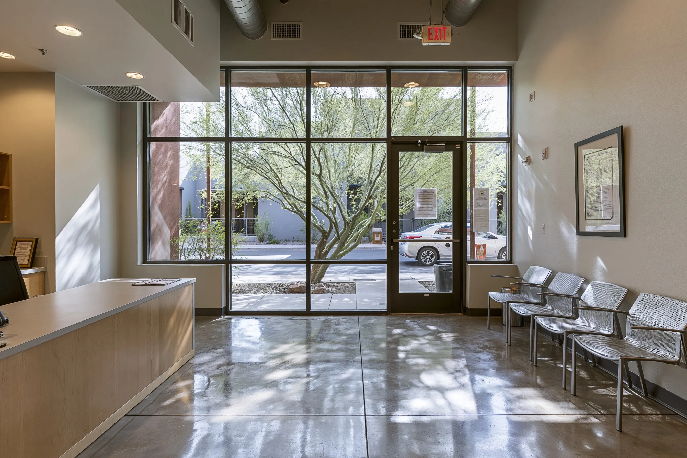 Small office reception with a satin polished concrete floor, a plain desk, waiting chairs and a glass entrance with a palo verde tree outside